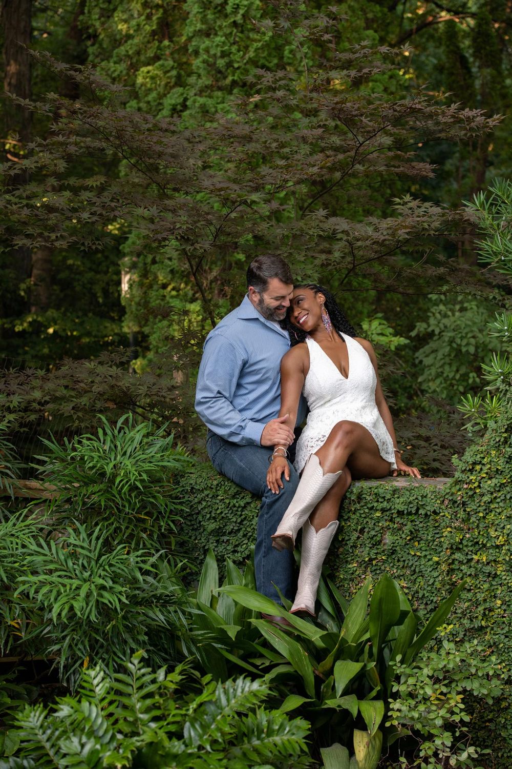 A couple shares an intimate moment among lush green foliage in a romantic garden setting.