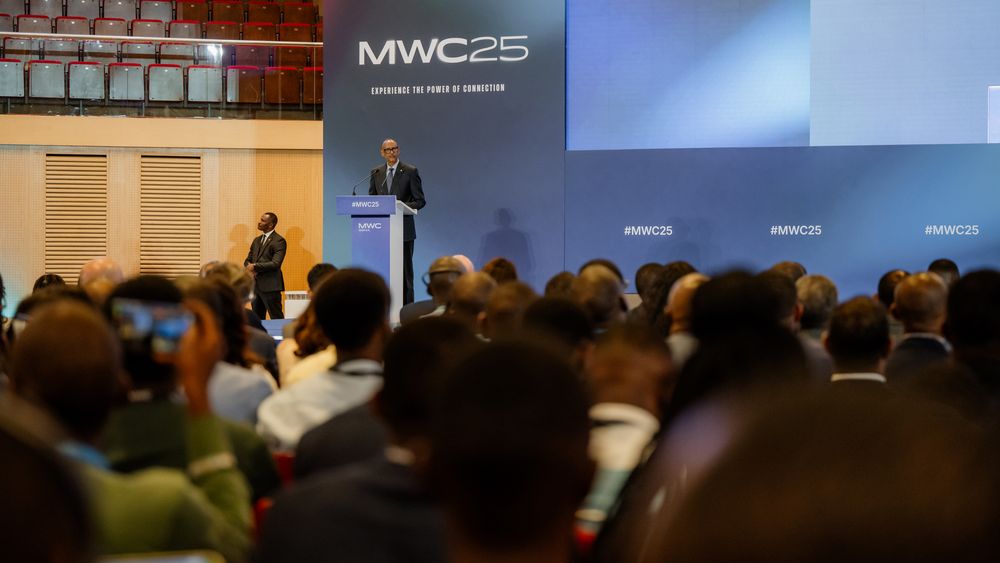 A speaker presents at MWC25 conference to a packed audience in an auditorium with blue stage backdrop.