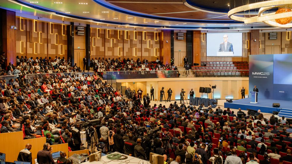 Large audience fills a modern conference hall with curved seating rows during a business presentation event.