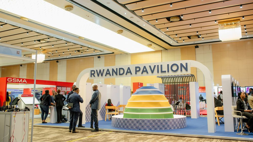 Colorful Rwanda Pavilion exhibit with rainbow-striped pyramid display and visitors at a convention center.