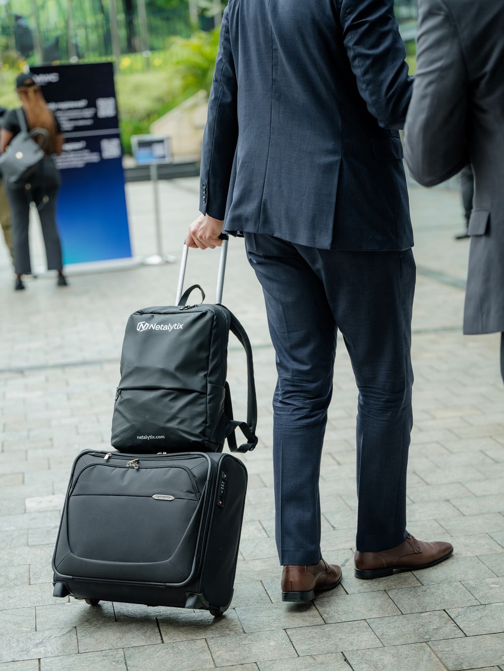 Business travelers with black rolling suitcases and bags wait in line at a professional event.