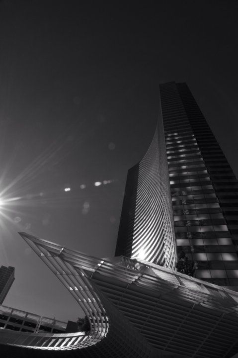 Black and white low angle shot of a skyscraper with dramatic sunburst and architectural canopy.