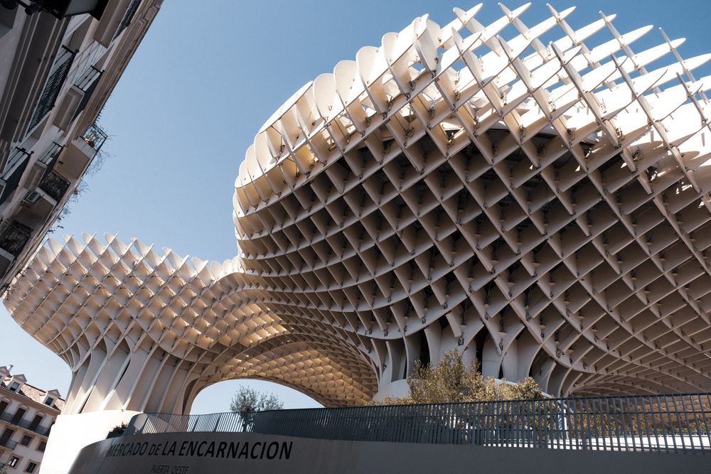 Close-up view of the Metropol Parasol structure in Seville, Spain, featuring its distinctive latticed wooden canopy against a blue sky.
