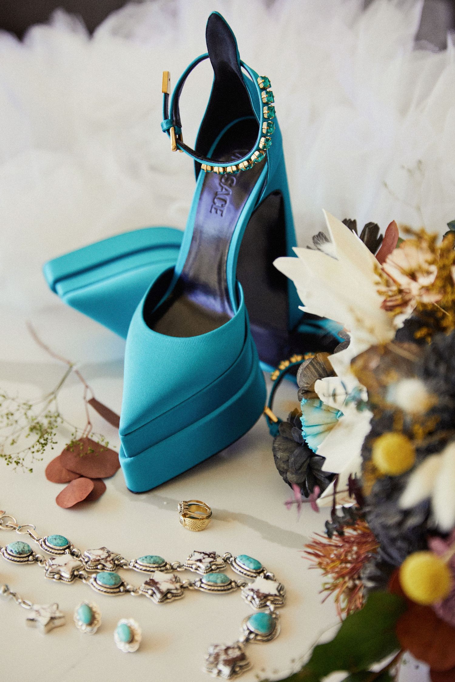 Teal blue wedding shoes arranged with matching jewelry and floral accessories.
