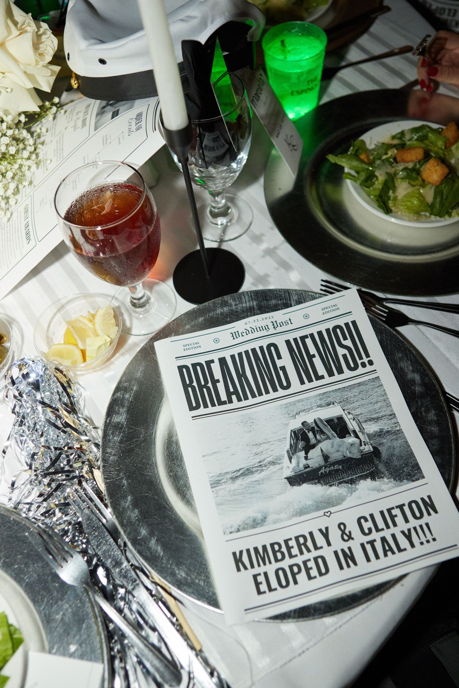 Custom wedding newspaper announcements displayed on a dining table with drinks and plates.