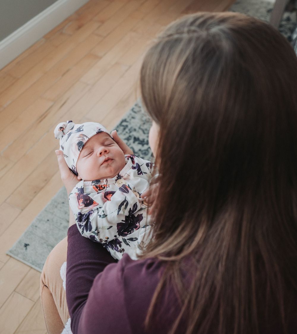 A newborn, wrapped in a floral onesie, is lovingly looked at by her mother.