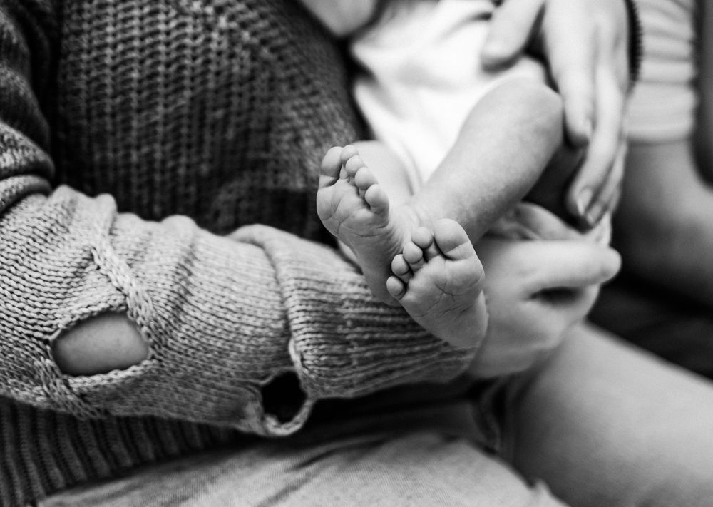 Black and white close-up photo showing a baby's tiny feet sticking out while behind held by his mom.