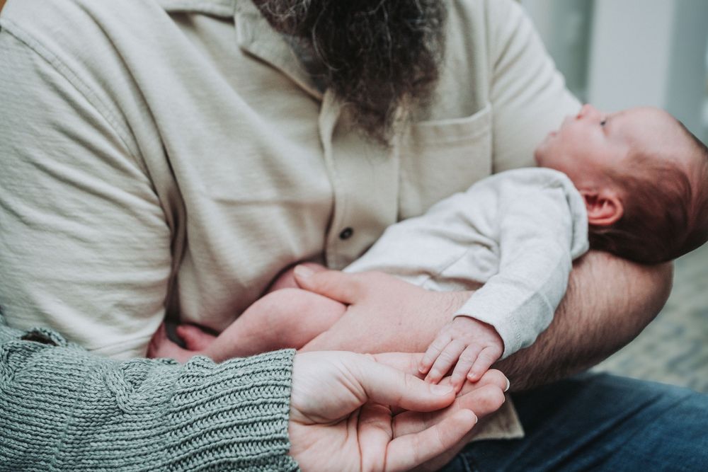 A newborn baby looks up at his dad while being held.  Meanwhile, the baby's mom is holding his hand.