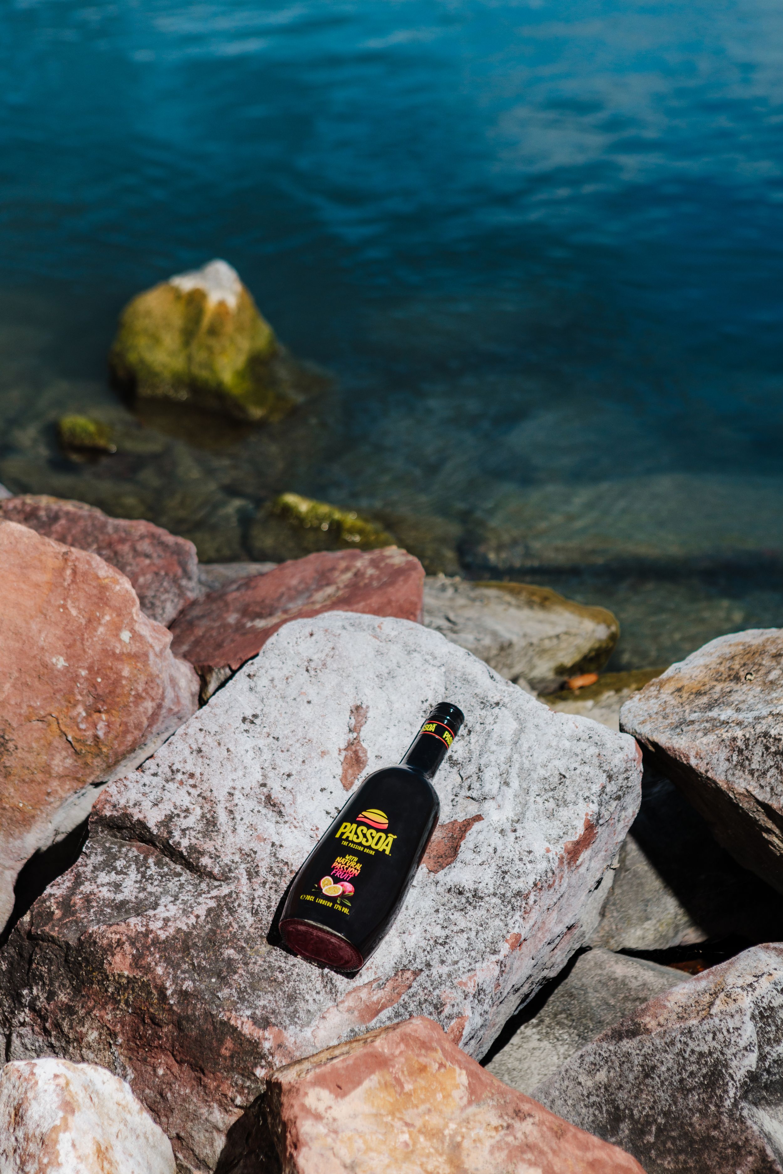 A dark bottle resting on coastal rocks with turquoise water in the background.