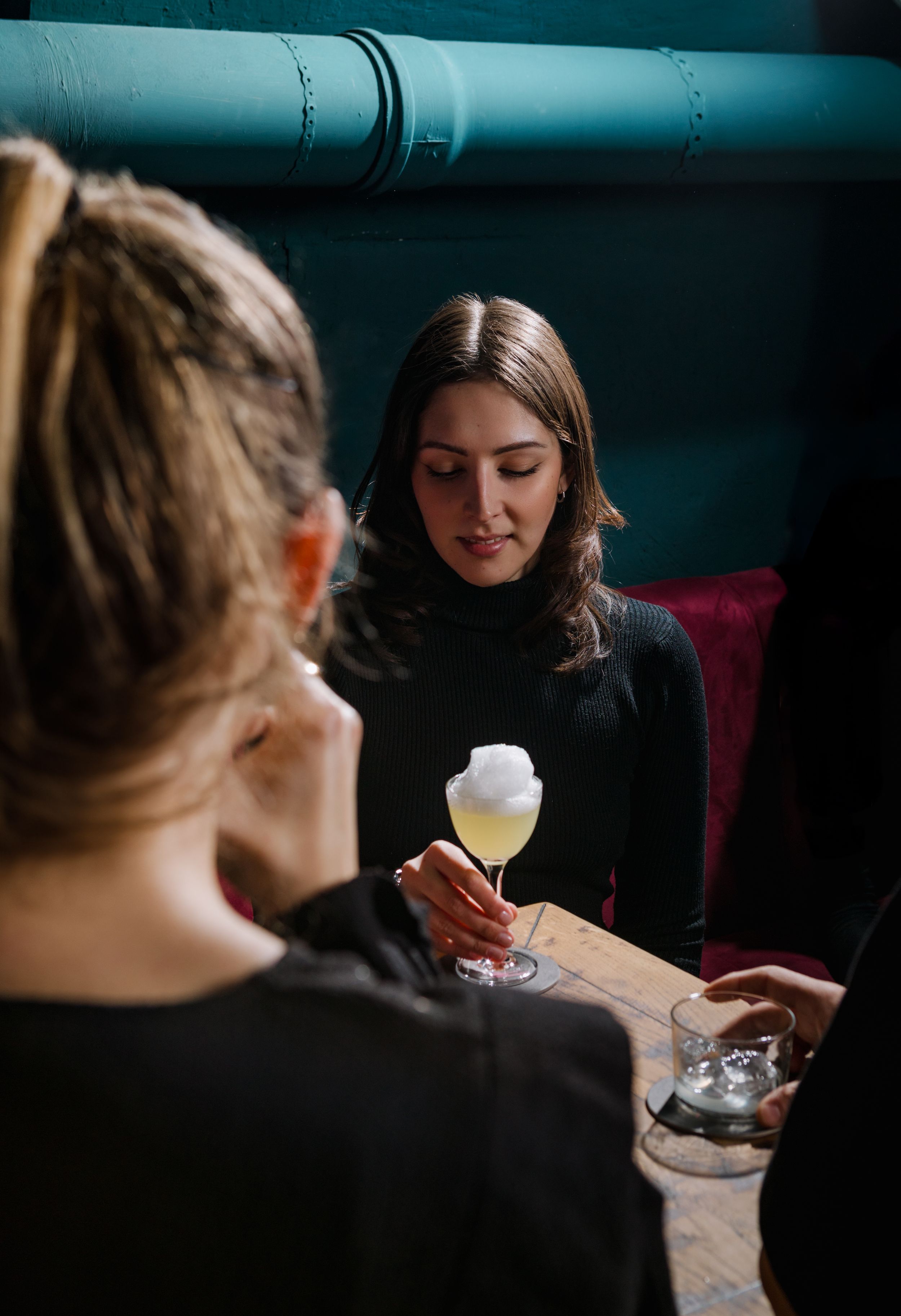 Two people enjoying cocktails in a dimly lit bar setting with industrial decor.