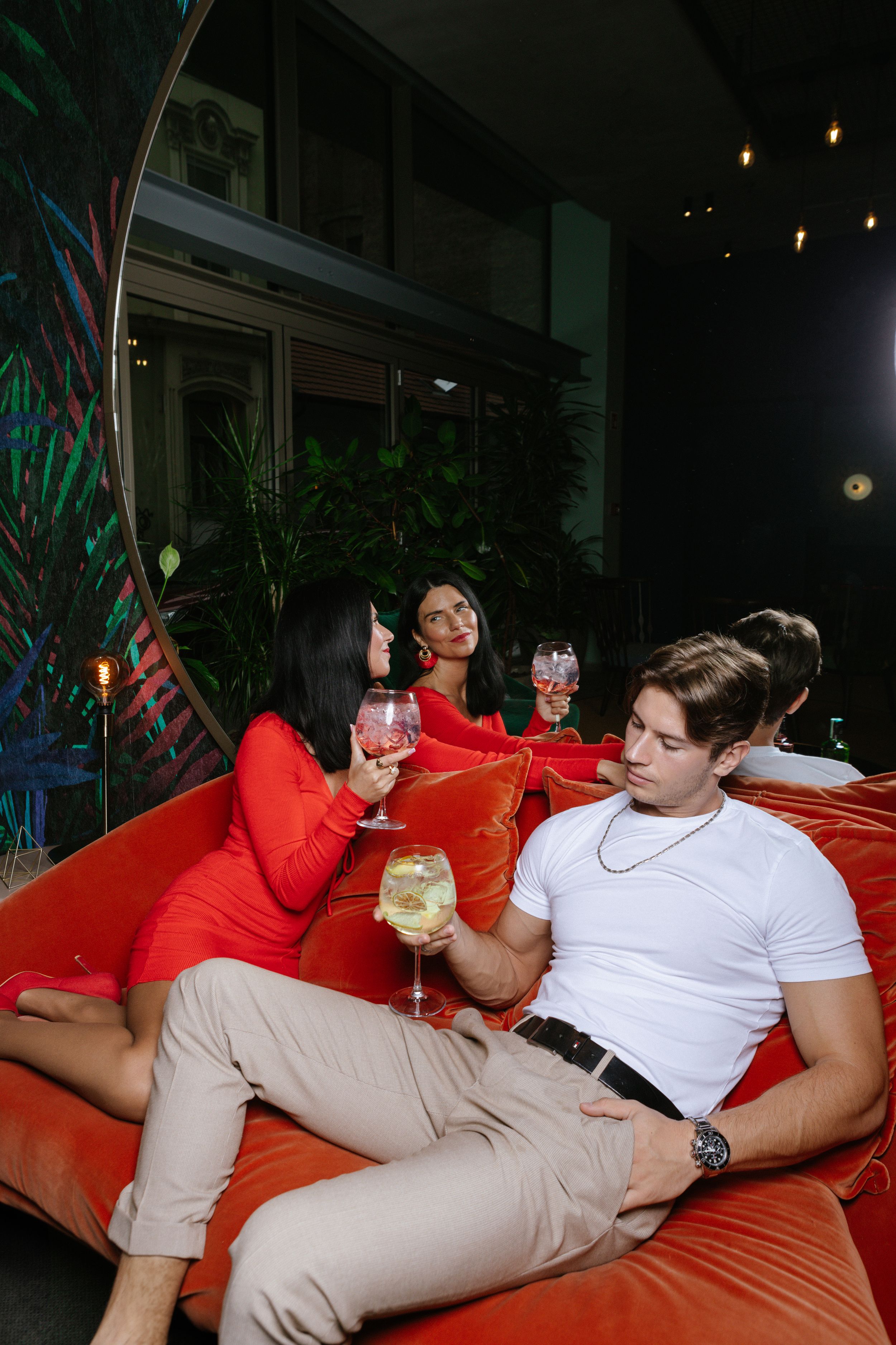 People relaxing with drinks on a red couch in an evening lounge setting.