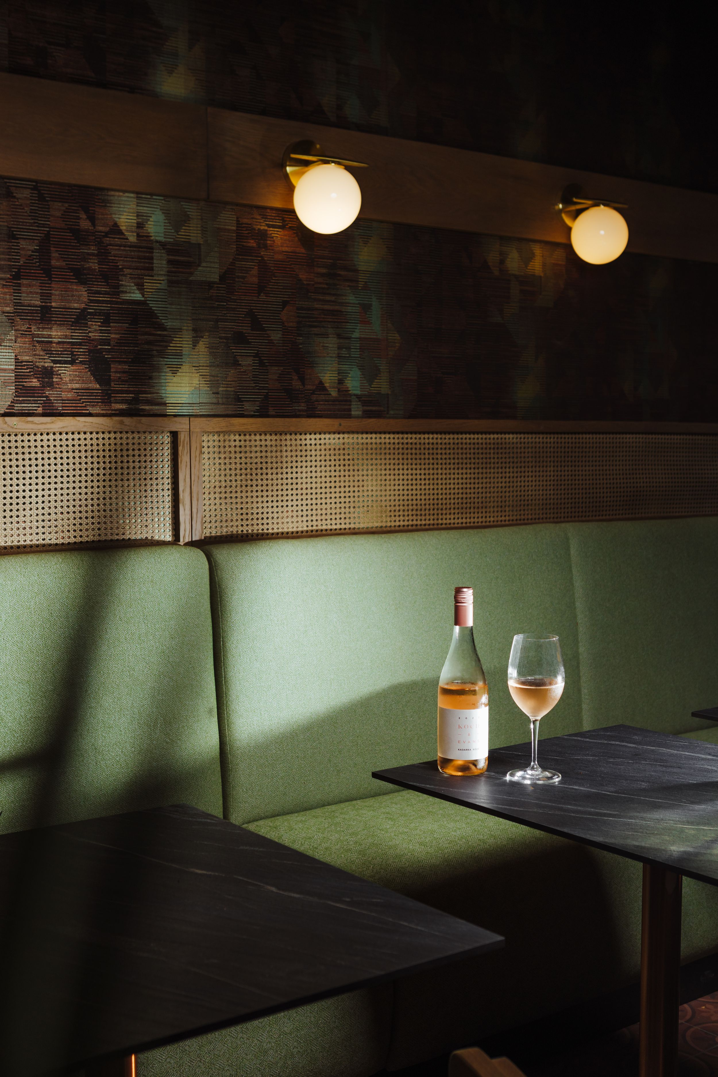 Elegant restaurant booth with green bench seating and a bottle of wine in moody lighting.