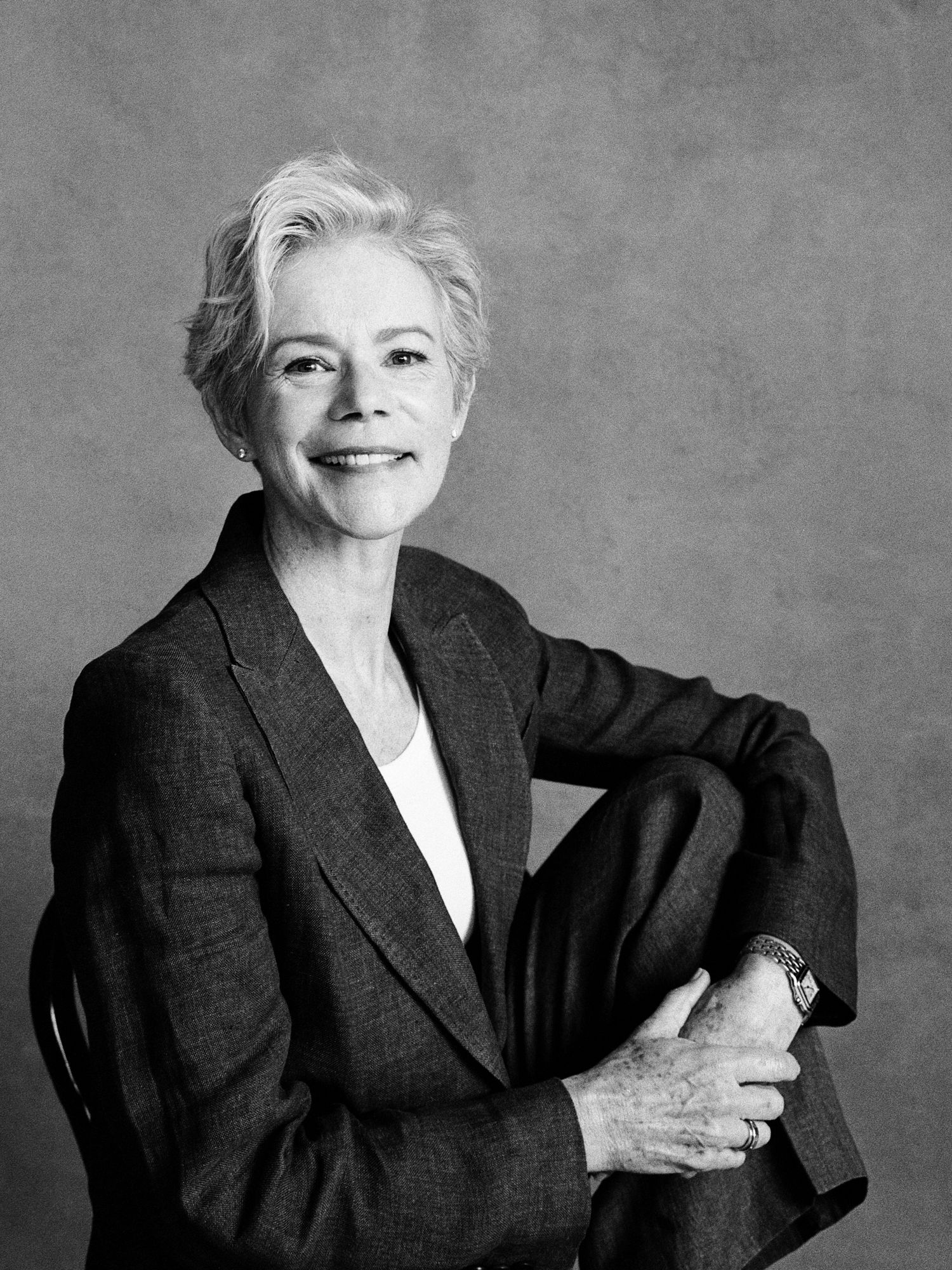 Elegant older woman with short gray hair smiling in a blazer, seated in a classic black and white portrait photo.