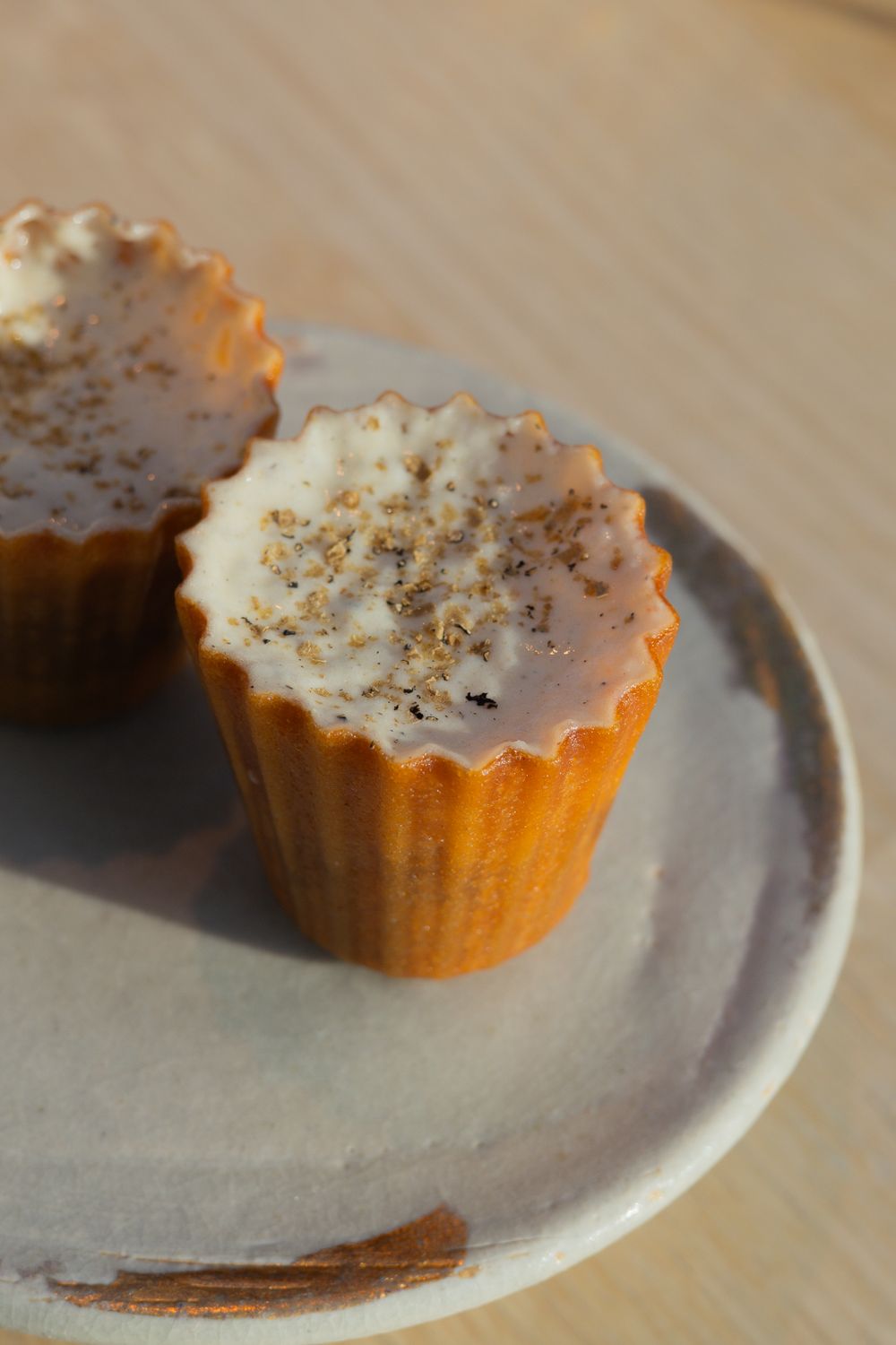 Mini cupcakes with cream frosting and gold dust garnish on a ceramic plate.