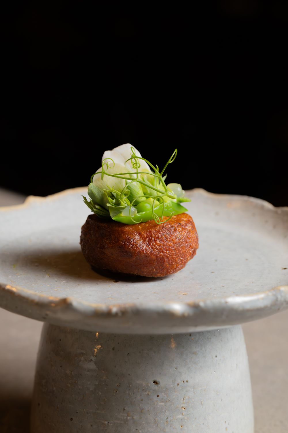A round pastry garnished with fresh greens and cream on a raised ceramic pedestal.
