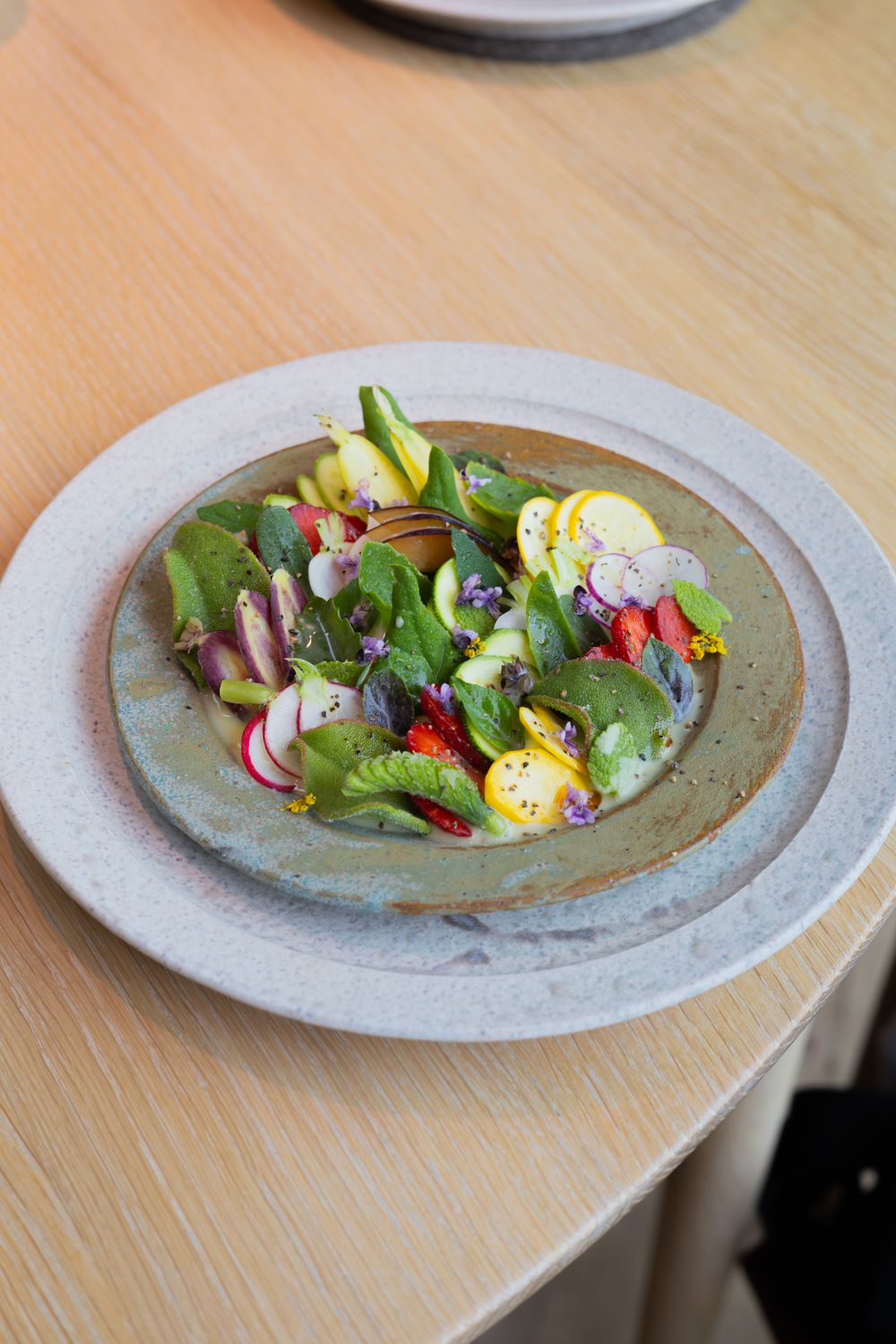 Fresh salad with colorful vegetables, eggs, and edible flowers plated on a gray ceramic dish.