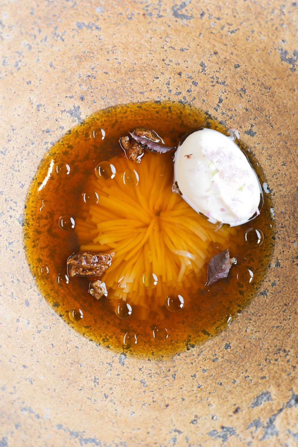 A golden broth with a radial pattern and small bubbles, topped with a dollop of white cream in a rustic bowl.