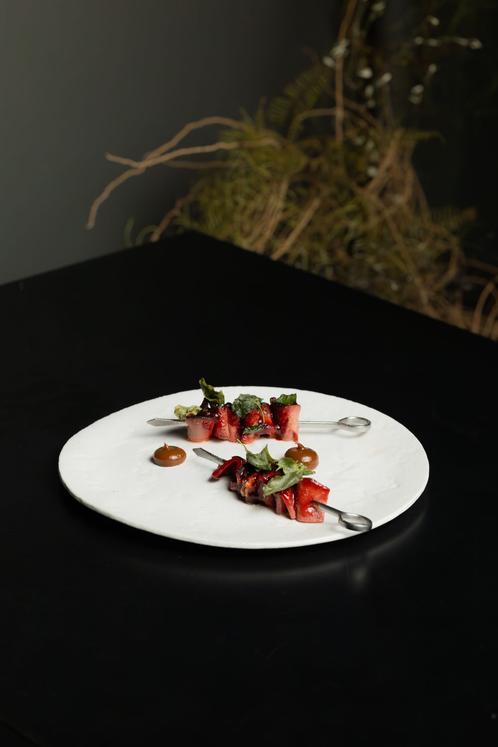 Artistically plated red meat dish with decorative sauces on a white plate against dark background.