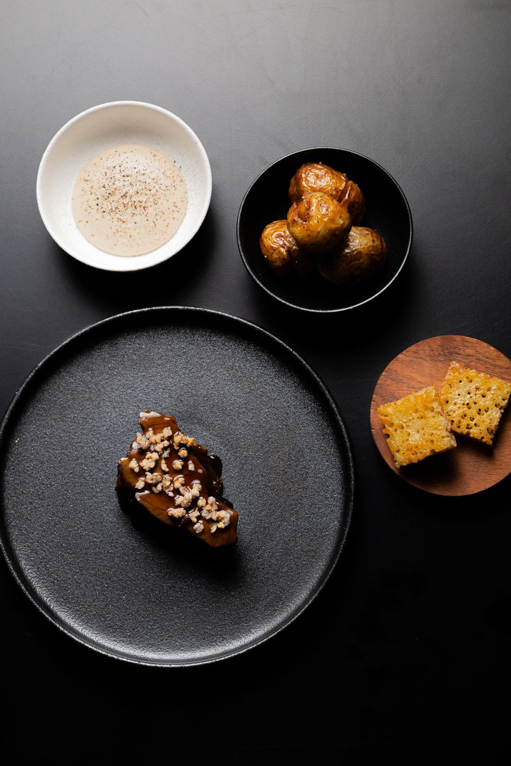 Modern plating of fine dining dishes on black and white plates against a dark background.
