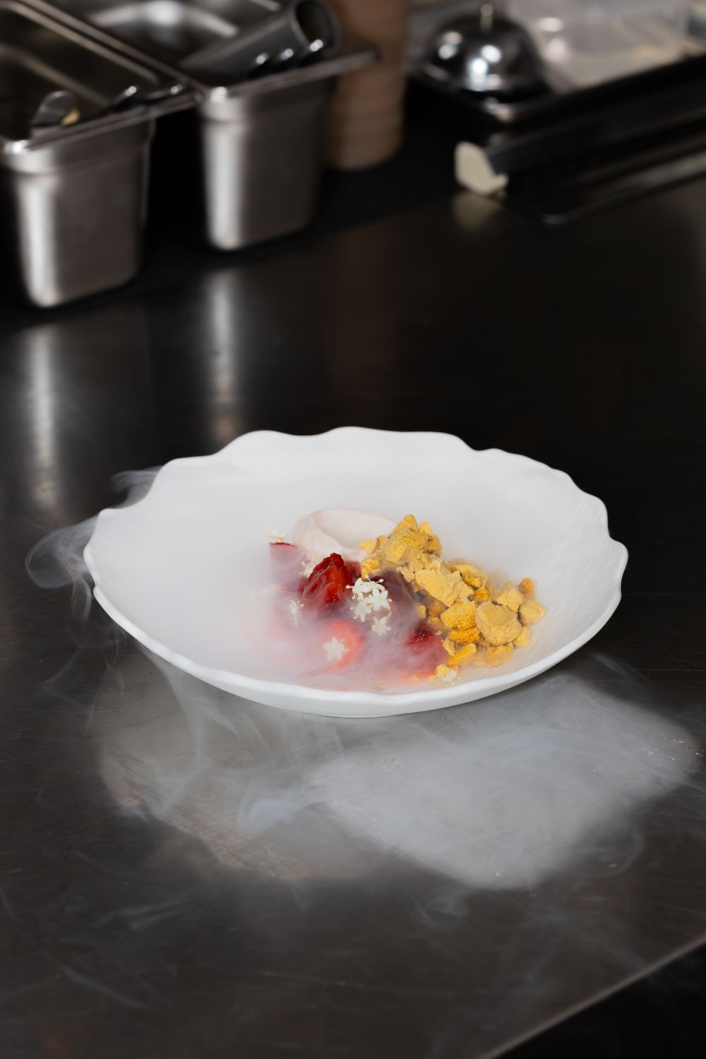 A white plate with colorful food elements surrounded by dramatic smoke on a dark surface.