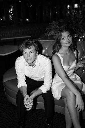 A black and white photo of a couple seated at a formal event, with the woman wearing white and man in dress shirt.