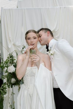 A romantic wedding couple shares an intimate moment against a white backdrop with floral decor.