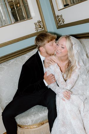 A couple shares a romantic moment on an elegant settee, with the bride wearing a beautiful lace gown and veil.