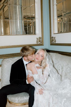 A romantic moment captured on an elegant white couch as a couple shares a tender kiss on their wedding day.