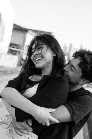 Candid black and white photos show a couple embracing and laughing together outdoors.