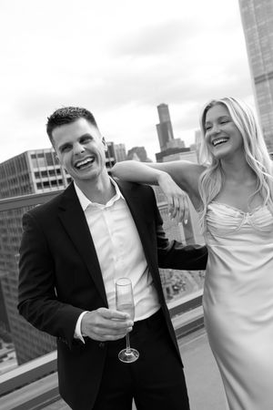 Couple enjoying champagne and laughter on a rooftop with urban skyline views.