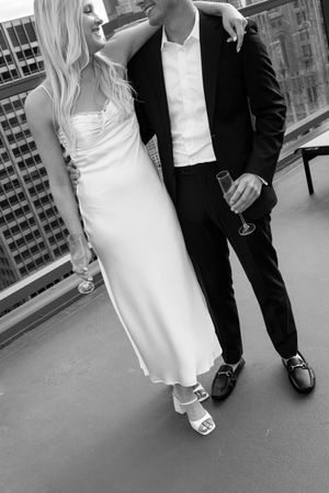 Black and white photo showing elegant couple's formal attire details on city rooftop.