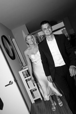 Black and white indoor photo of couple in formal attire walking through hallway.