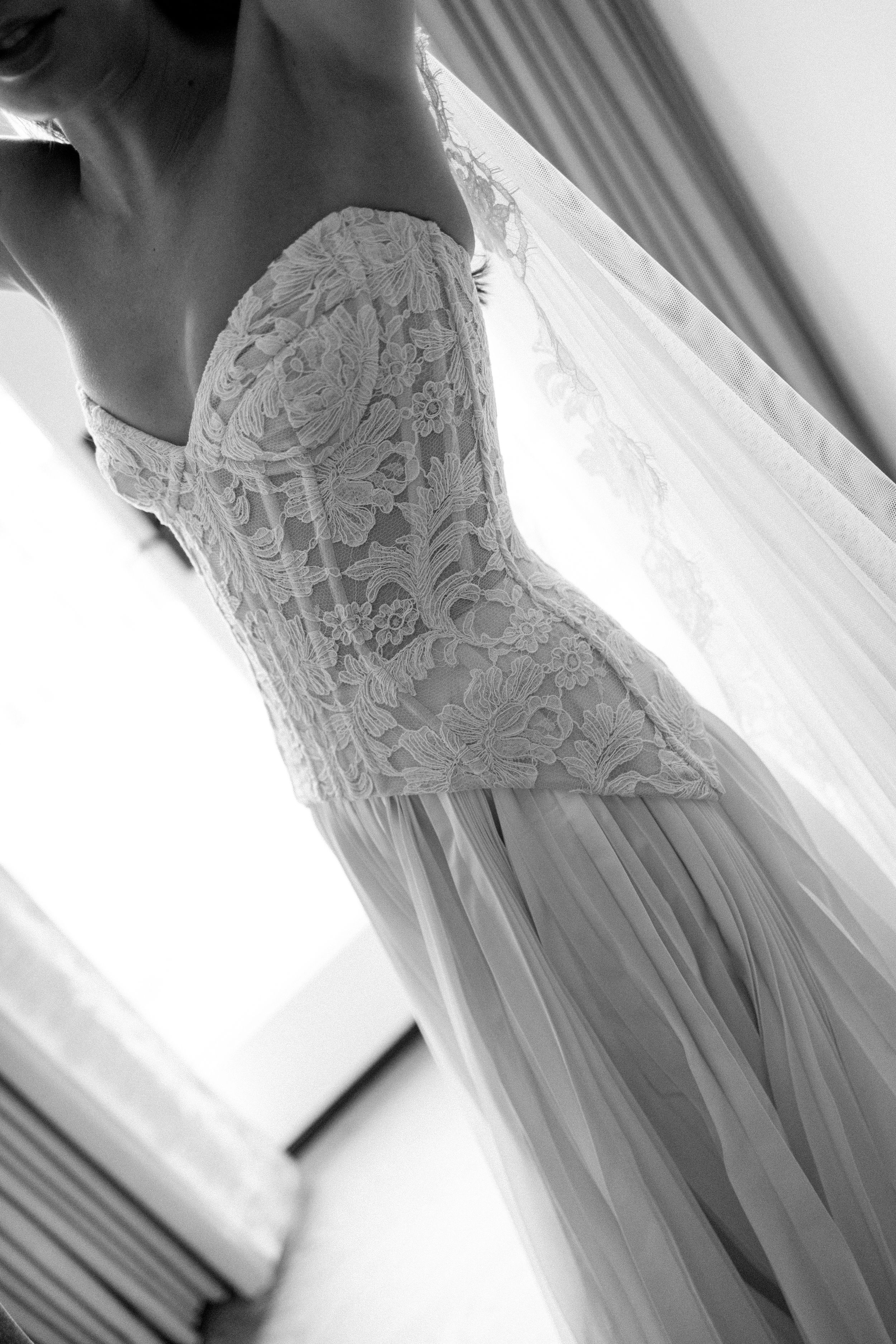 Black and white photo of a bride wearing an elegant strapless lace corset wedding gown with flowing chiffon skirt.