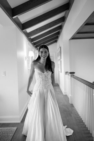 Smiling bride in strapless lace wedding gown stands in elegant hallway, black and white photo.
