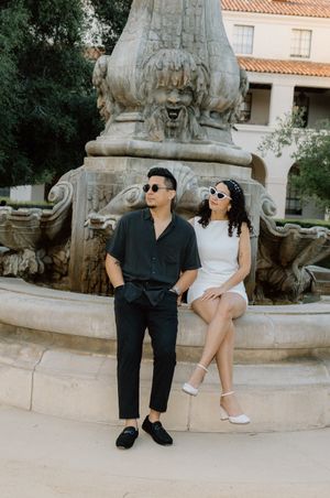 A couple in contrasting black and white outfits posing by an ornate stone fountain.