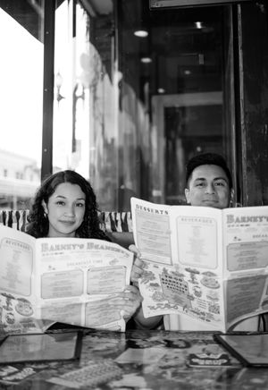 A vintage black and white photo of a couple reading menus together at a restaurant.