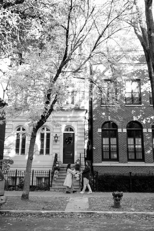 Black and white photo of historic brownstone townhouses with arched windows and trees lining a residential street.