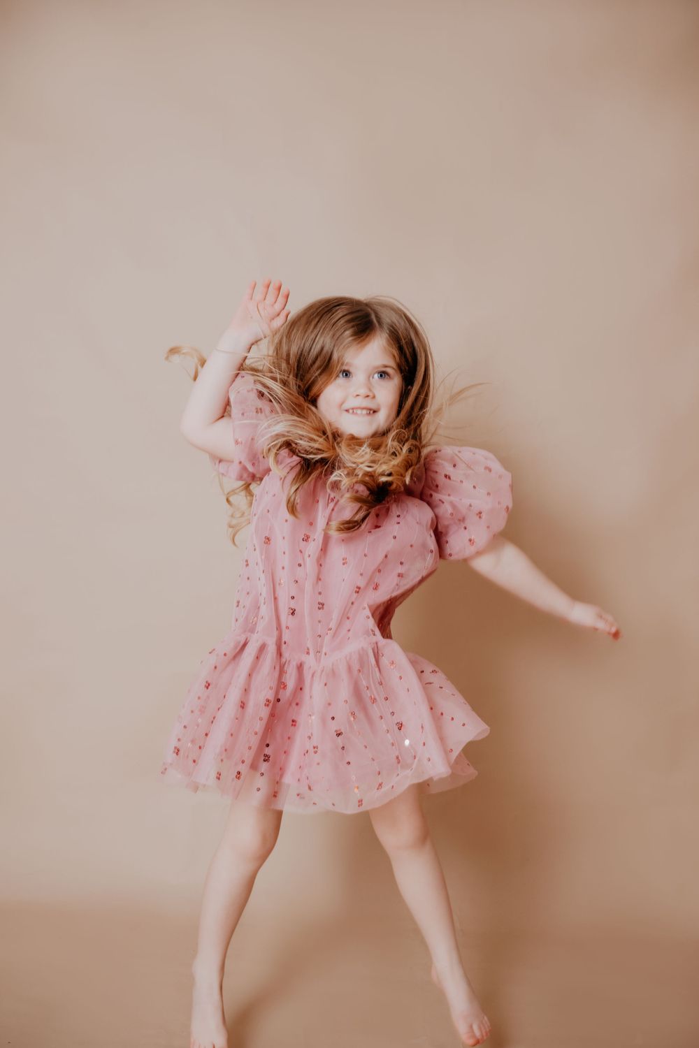 Child dancing and jumping in pink dress during playful photo session.