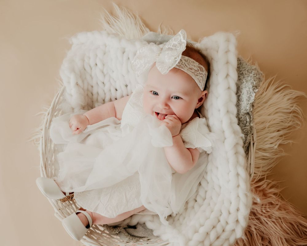 A baby wearing white lying in a cozy knit basket with soft textiles.