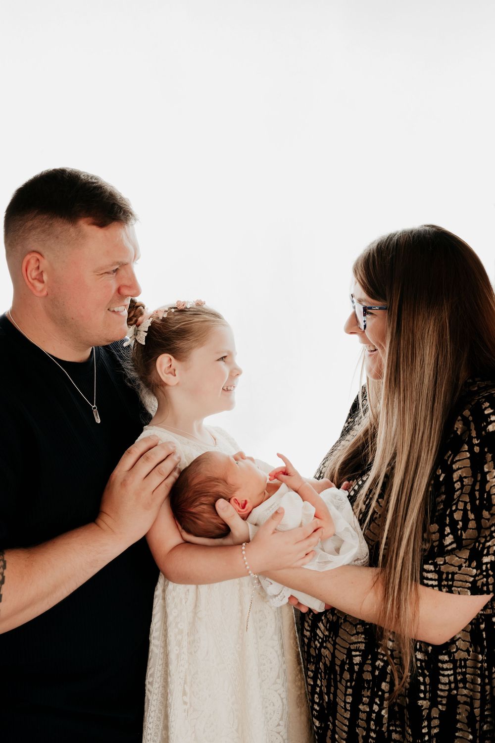 Happy family of four with parents and young daughter admiring their newborn baby indoors.