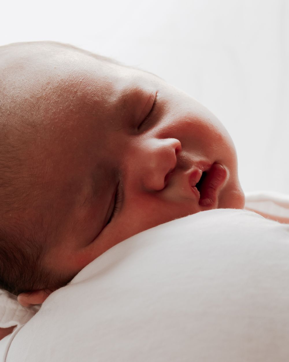 Peaceful sleeping newborn baby with tiny lips slightly parted resting on white surface.