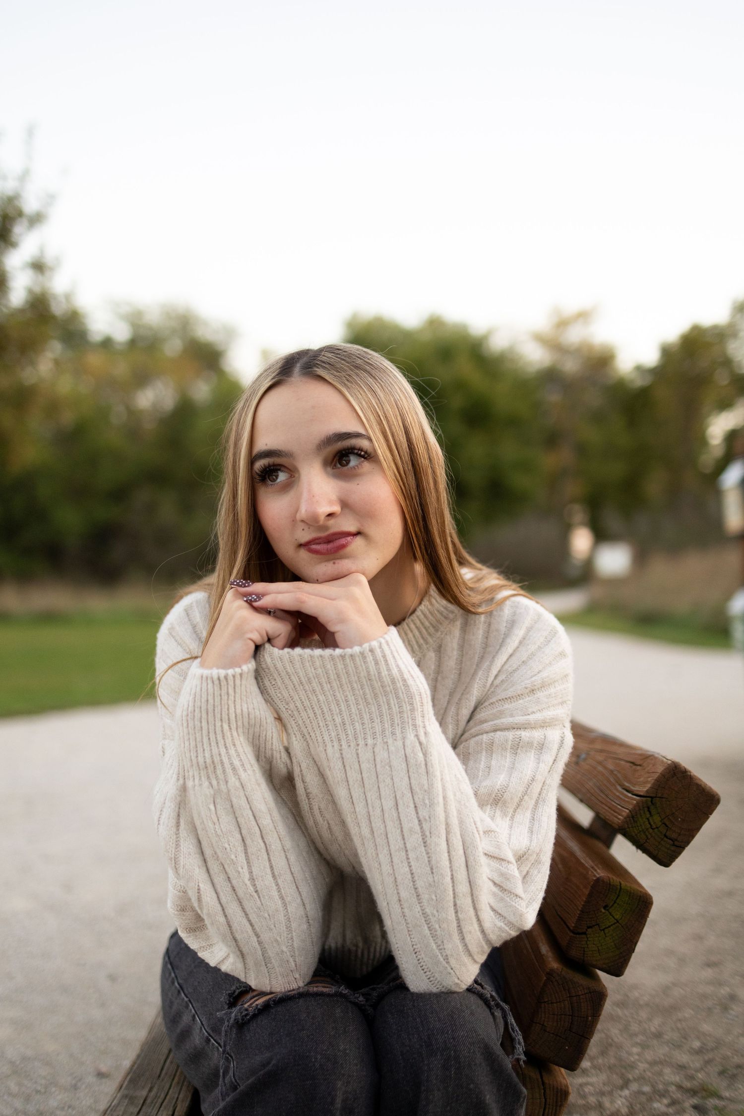 Sioux City, Iowa photographer. Blonde teenage girl in cream sweater sitting on wooden bench in an outdoor park.
