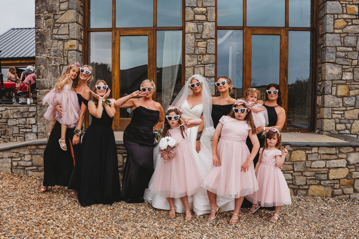 Wedding party poses in front of stone building wearing black and pink dresses.