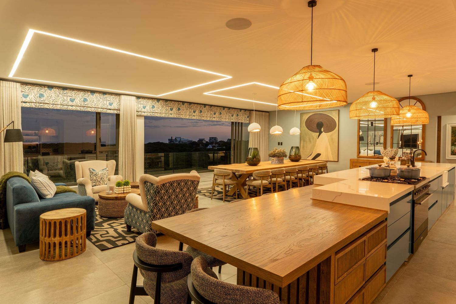 Modern open-plan kitchen and living area with wooden island, pendant lights, and sunset view.