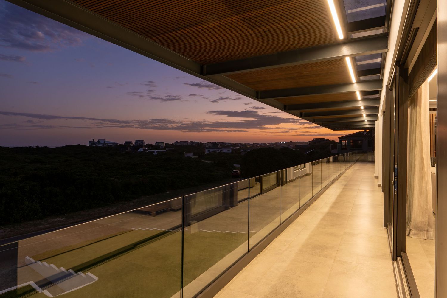 Sleek glass-railed balcony with LED ceiling lights overlooking a stunning purple dusk skyline.