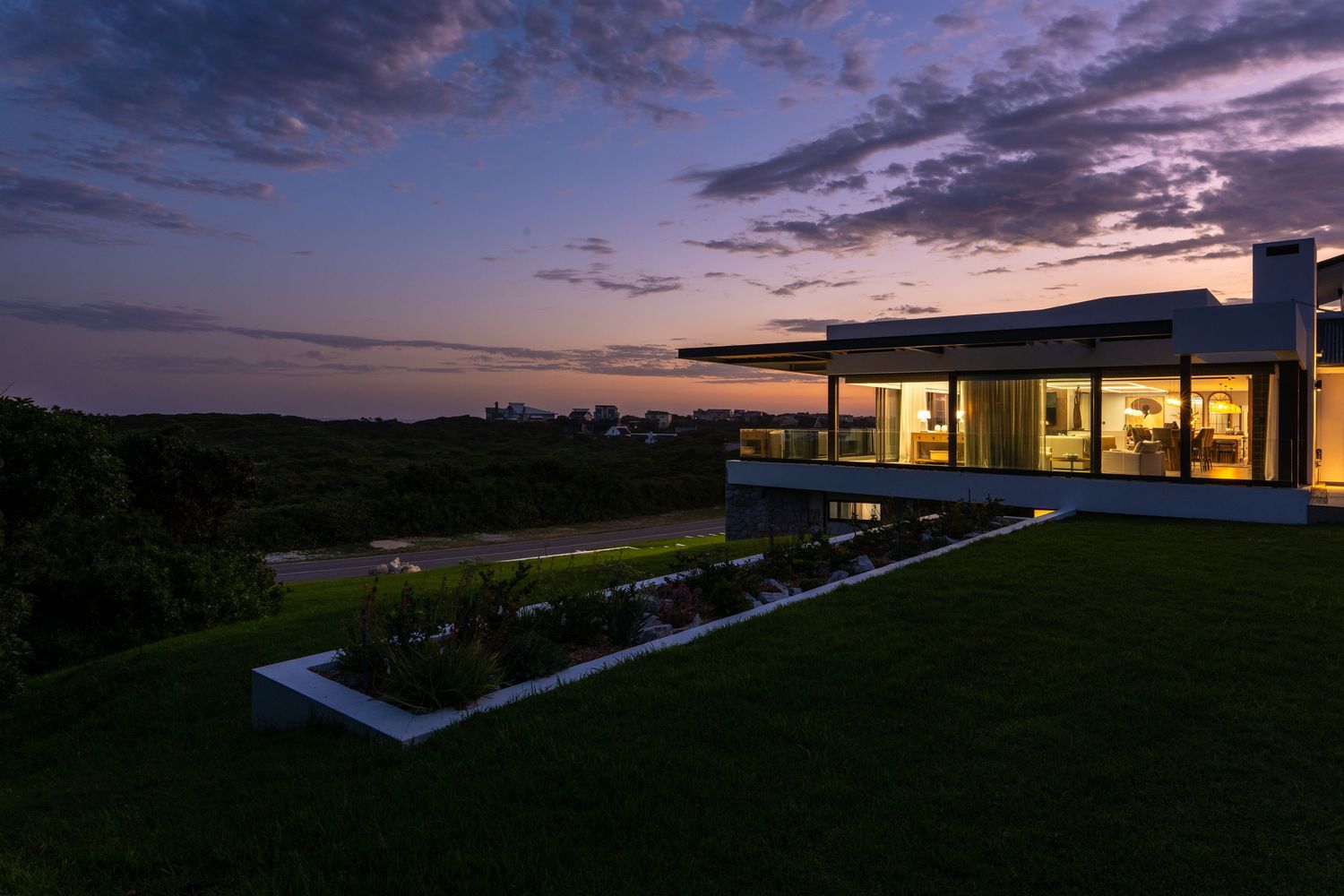 Modern luxury home exterior at dusk with glowing interior lights and dramatic purple sunset sky.