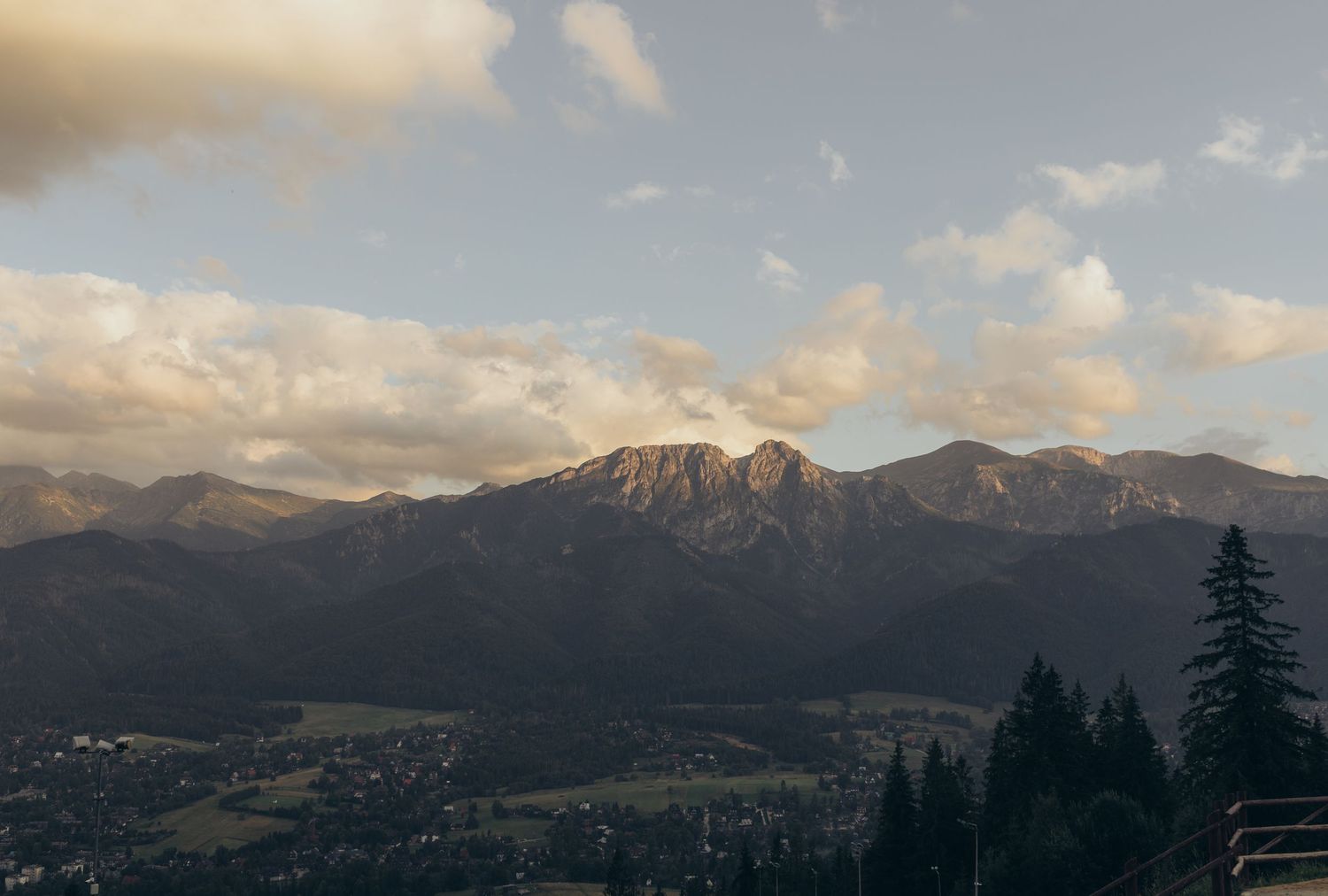 Dramatic mountain landscape at sunset with rugged peaks and forested slopes.