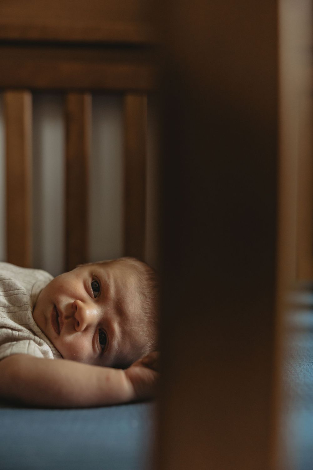 Baby smiling while lying down, viewed through wooden crib slats.