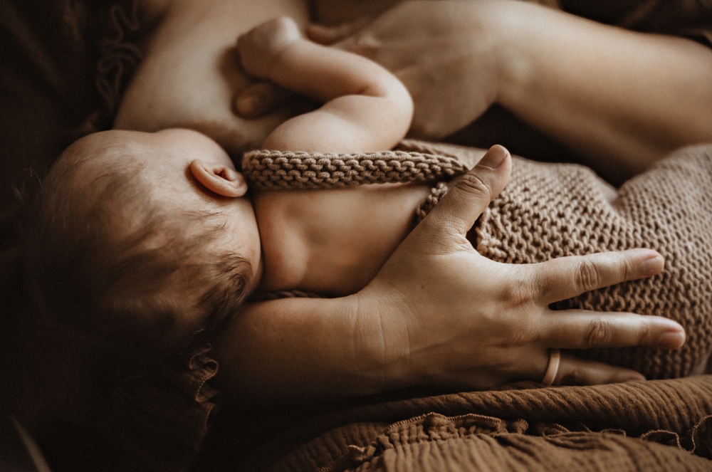Newborn baby lying on a brown knit blanket cradled in adult hands.