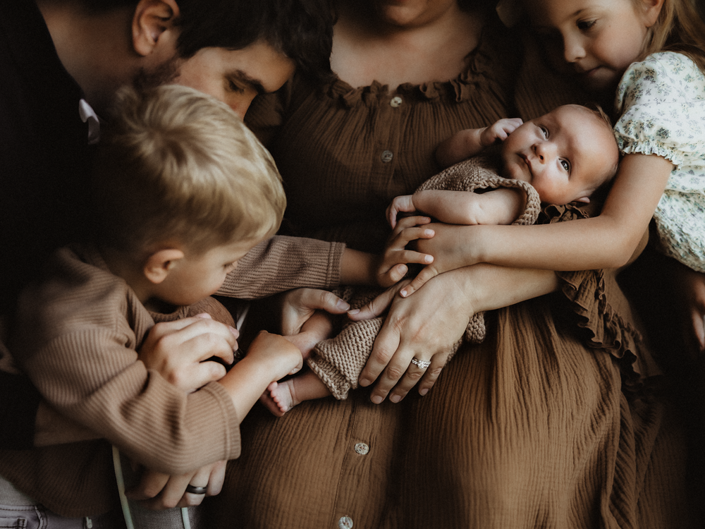 Family gathered closely around a newborn baby, with two young siblings gently touching the infant held by parents.